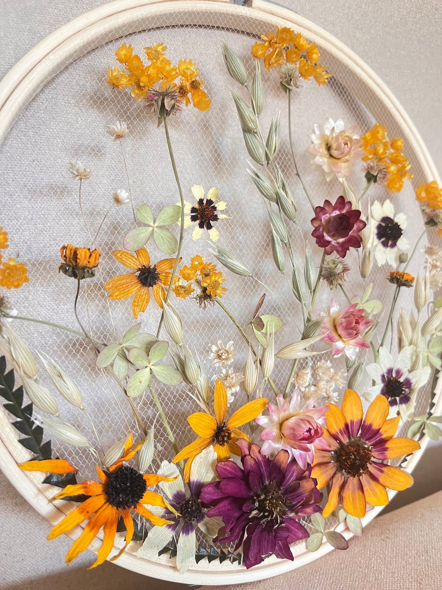 Real dried flowers are embroidered on tulle secured by an embroidery hoop. Dried botanicals include zinnias, starflowers, strawflowers and hydrangeas. The hoop is hung from the wall as a piece of wall art. Hoop is 8 inches in diameter.