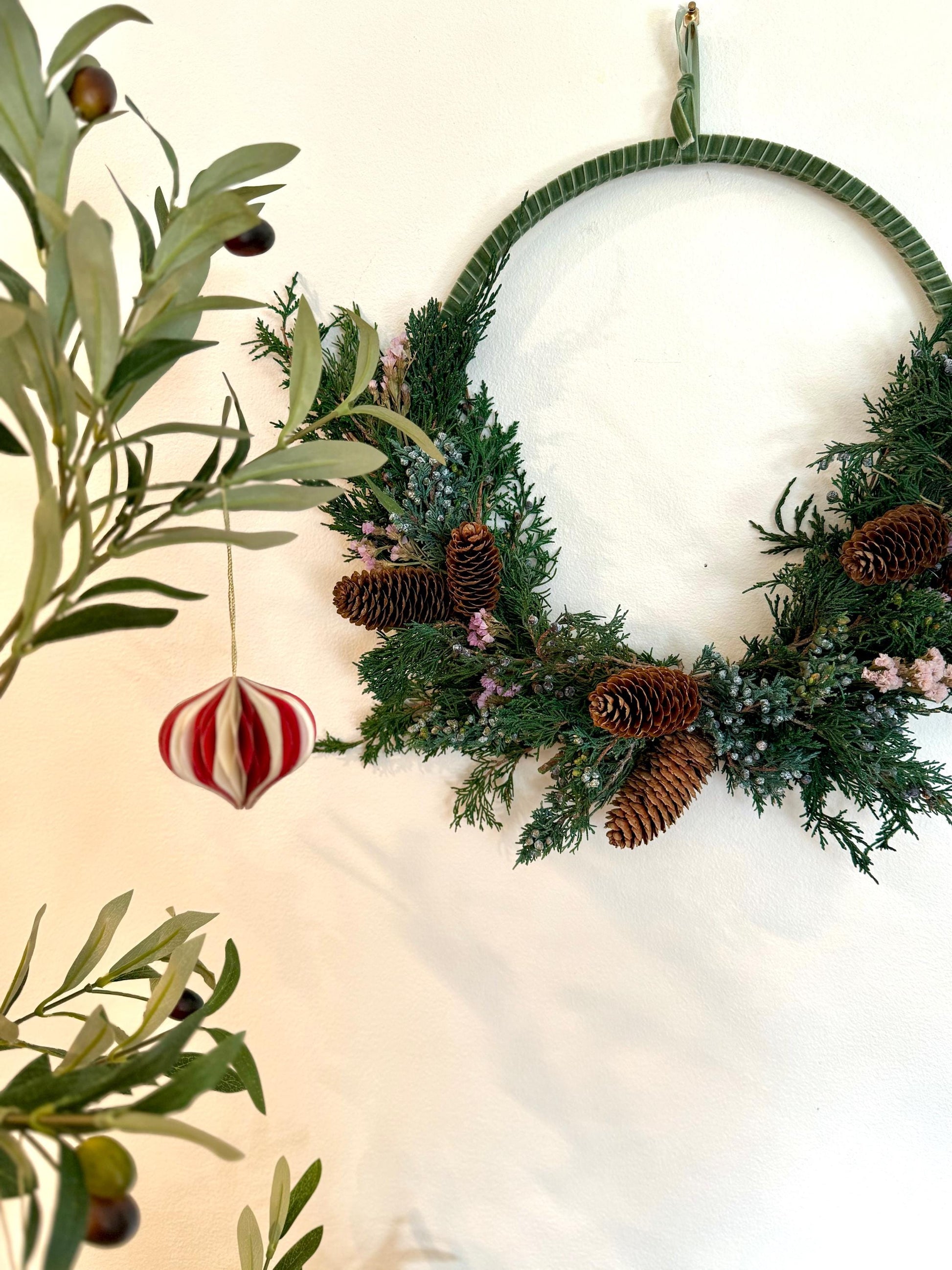 Holiday wreath featuring preserved juniper, lavender statice, pinecones and a beautiful pine green velvet ribbon. Adorn a wall, mantel or sheltered door; this dried flower wreath is the perfect addition to your holiday decor.