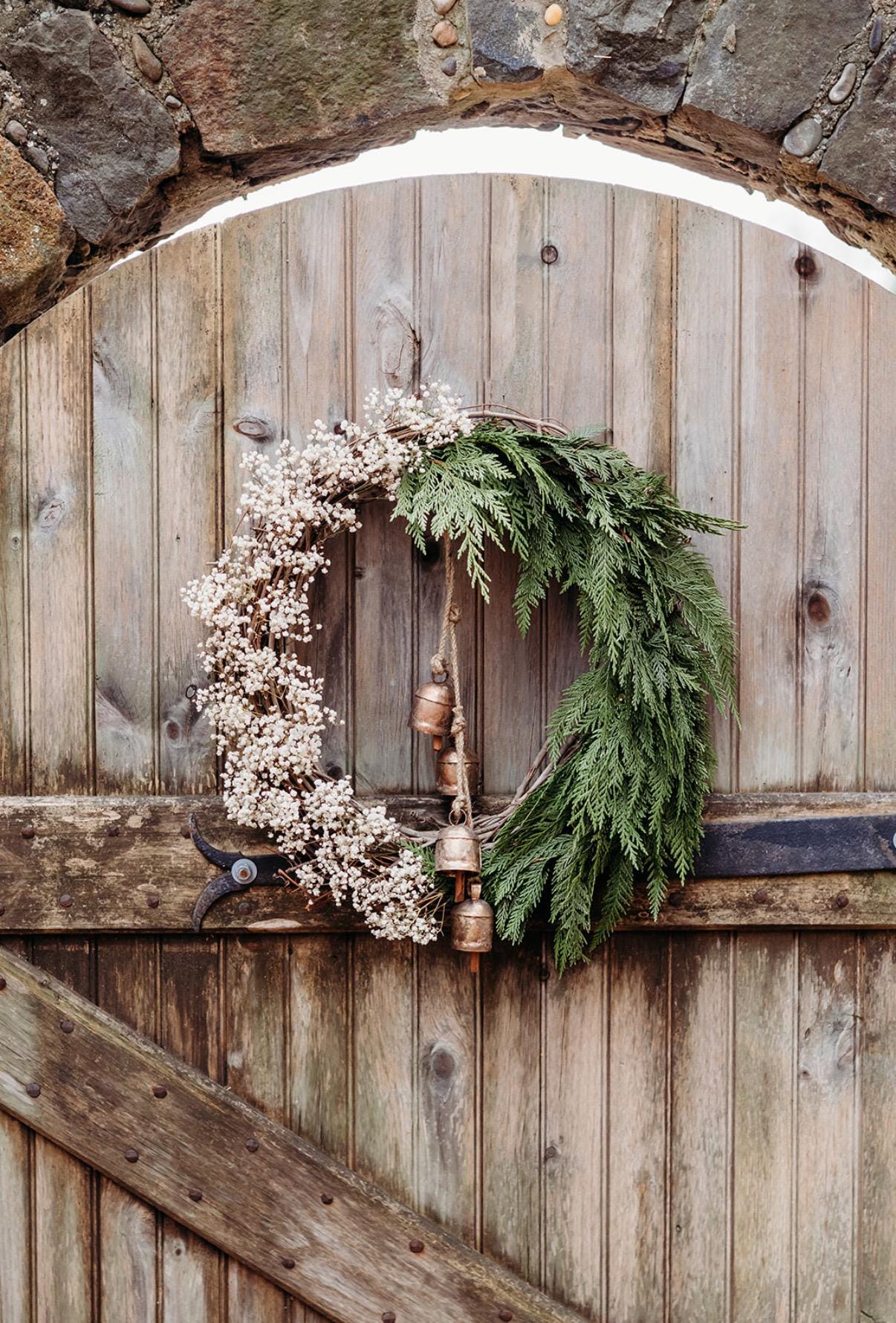 Holiday wreath featuring fresh cedar, preserved baby&#39;s breath and a hanging vintage copper bell cluster. Adorn a wall, mantel or sheltered door; this dried flower wreath is the perfect way to add beauty to your space this holiday season decor.