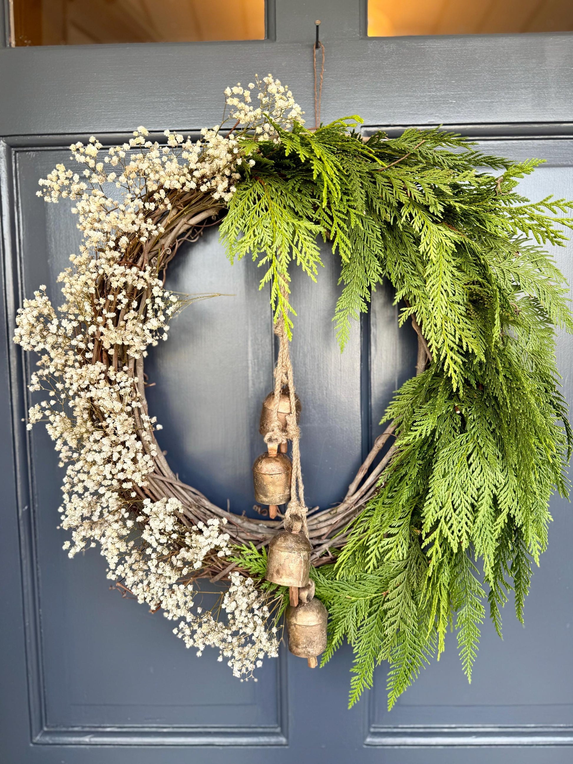 Holiday wreath featuring fresh cedar, preserved baby&#39;s breath and a hanging vintage copper bell cluster. Adorn a wall, mantel or sheltered door; this dried flower wreath is the perfect way to add beauty to your space this holiday season decor.