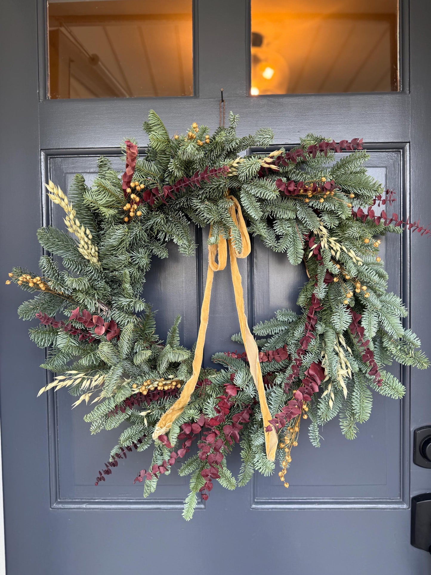 Holiday wreath featuring fresh noble fir, preserved eucalyptus, dried flax and  a gorgeous gold velvet ribbon. 
Adorn a wall, mantel or sheltered door; this fresh, dried and preserved wreath is the perfect way to add beauty to your space.