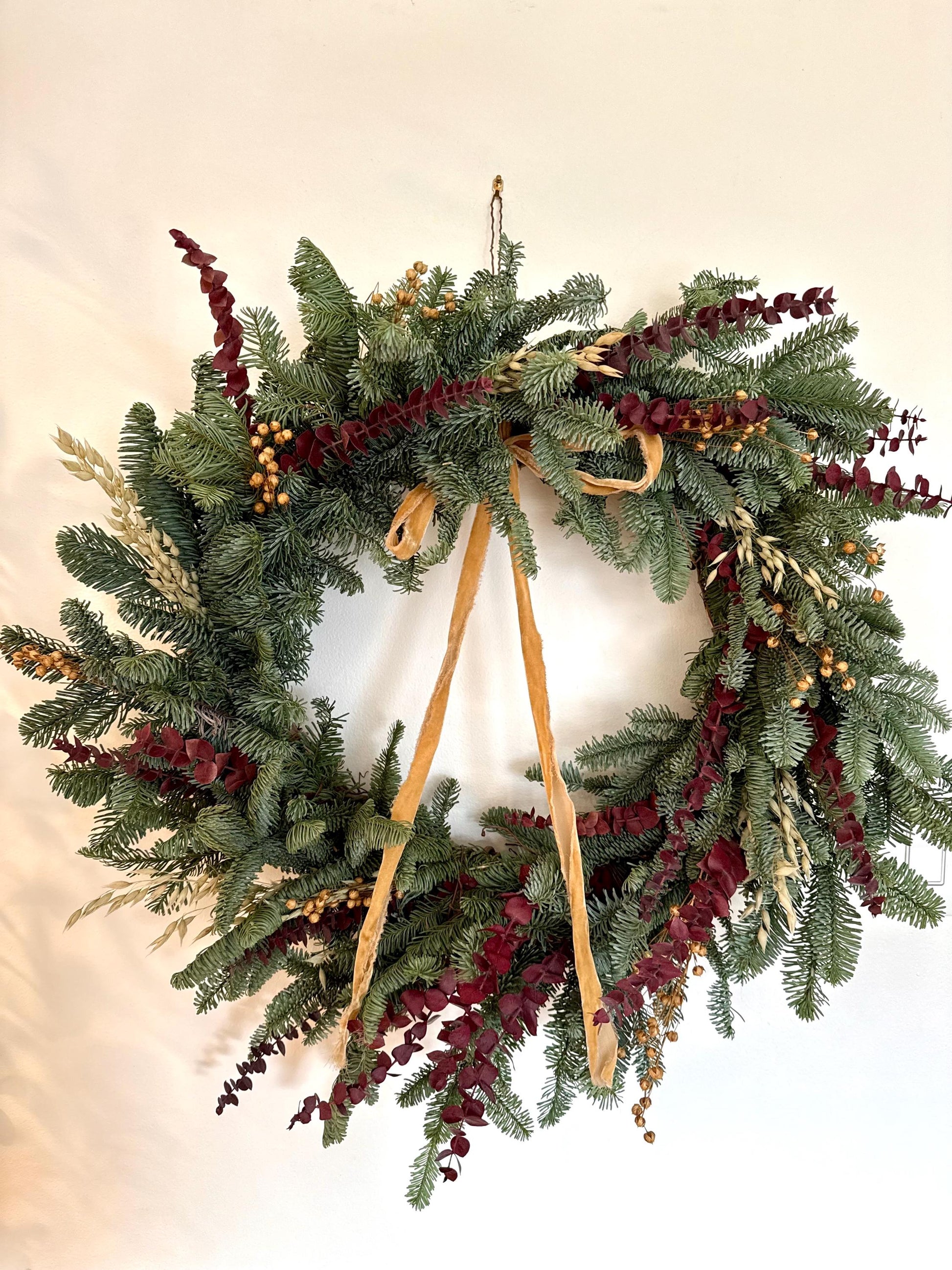 Holiday wreath featuring fresh noble fir, preserved eucalyptus, dried flax and  a gorgeous gold velvet ribbon. 
Adorn a wall, mantel or sheltered door; this fresh, dried and preserved wreath is the perfect way to add beauty to your space.