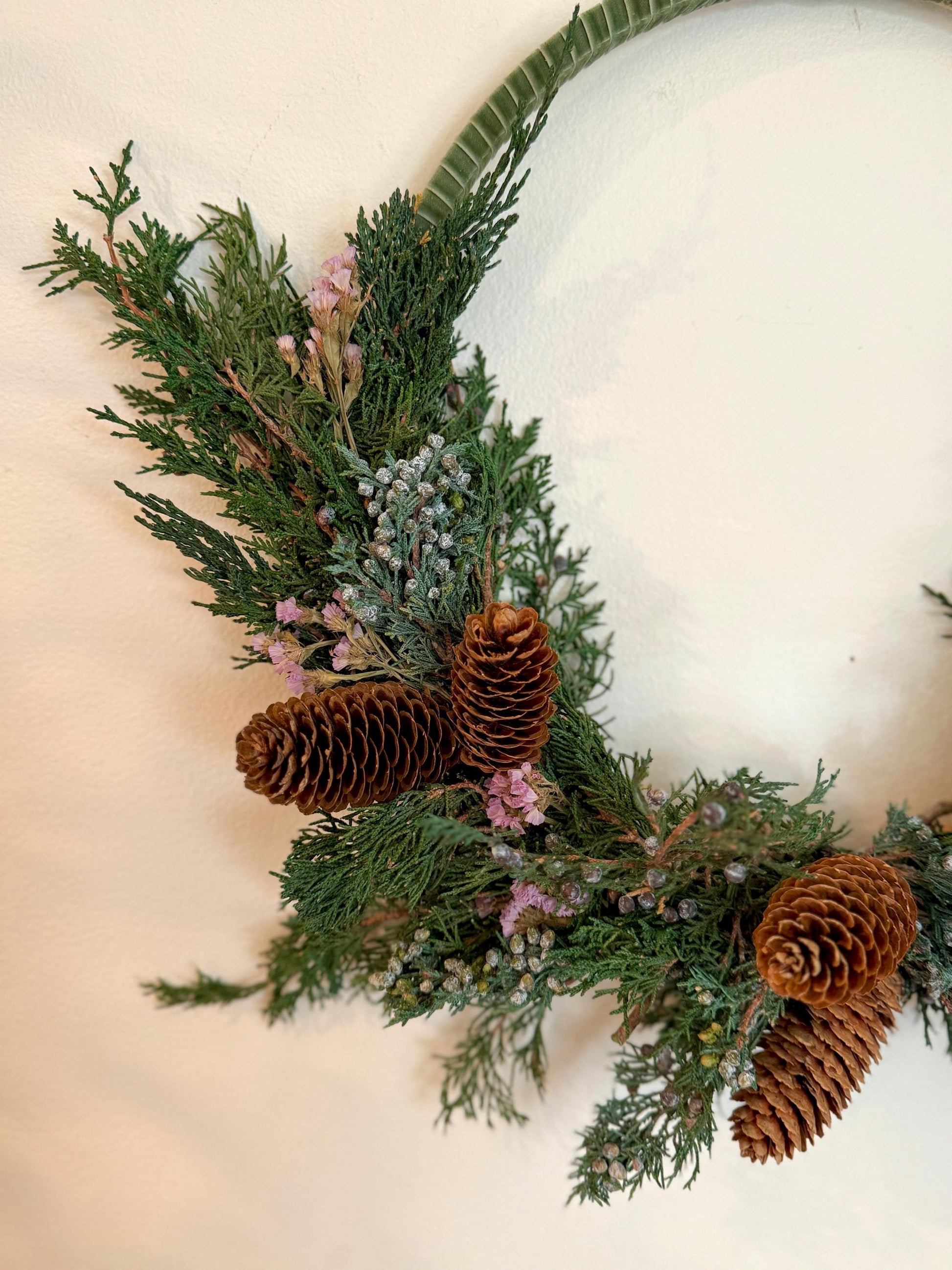 Holiday wreath featuring preserved juniper, lavender statice, pinecones and a beautiful pine green velvet ribbon. Adorn a wall, mantel or sheltered door; this dried flower wreath is the perfect addition to your holiday decor.
