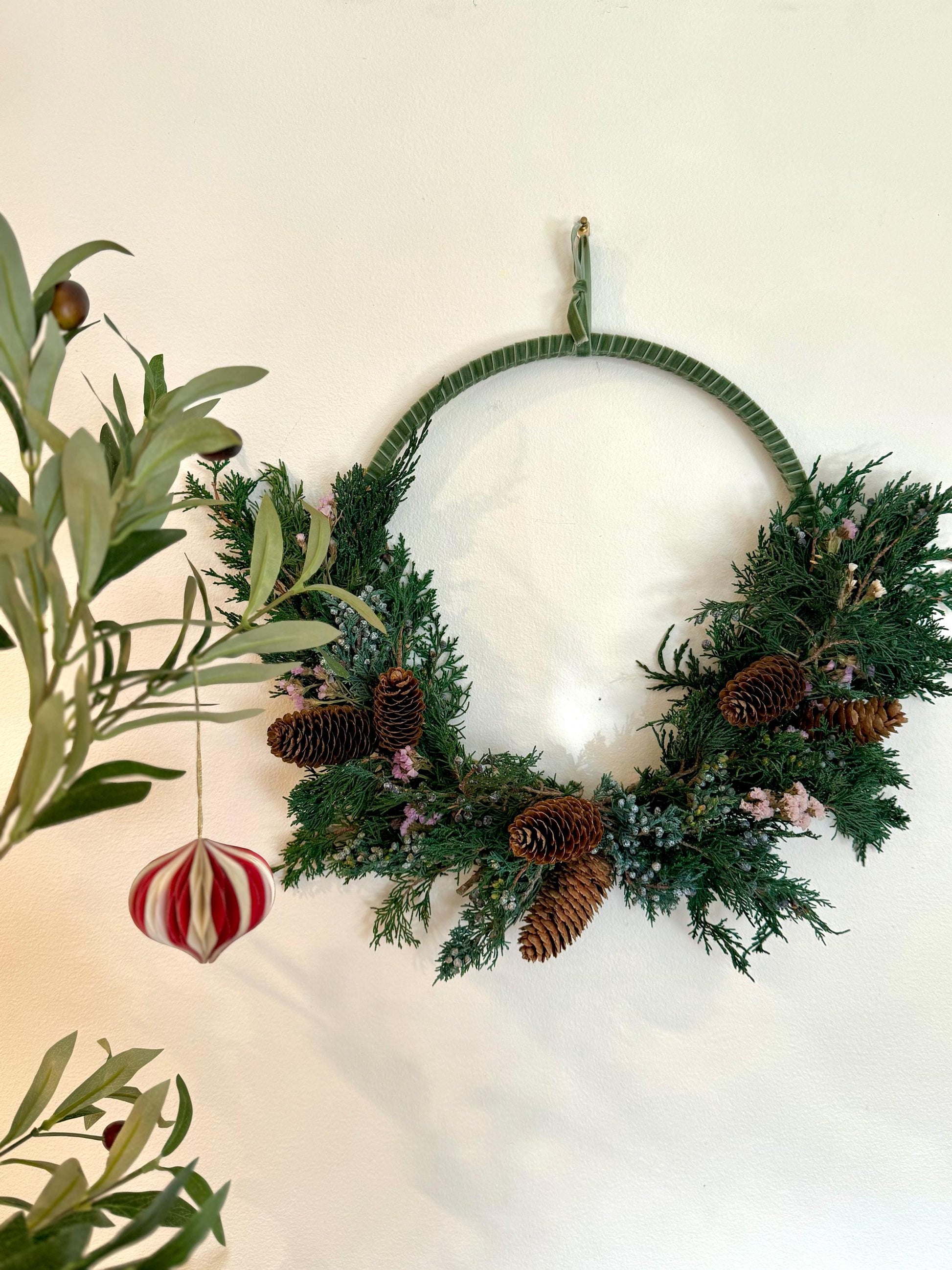 Holiday wreath featuring preserved juniper, lavender statice, pinecones and a beautiful pine green velvet ribbon. Adorn a wall, mantel or sheltered door; this dried flower wreath is the perfect addition to your holiday decor.