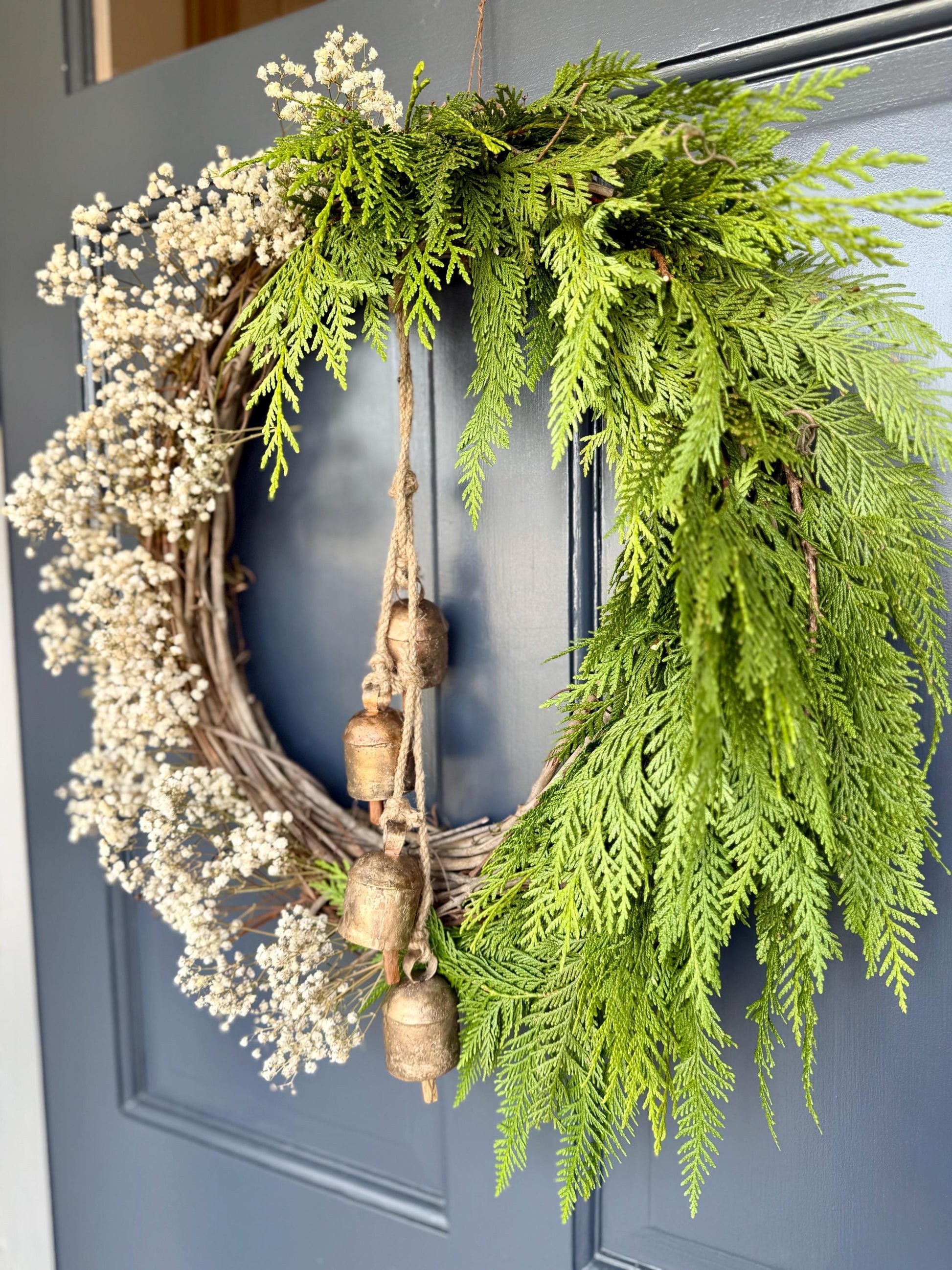 Holiday wreath featuring fresh cedar, preserved baby&#39;s breath and a hanging vintage copper bell cluster. Adorn a wall, mantel or sheltered door; this dried flower wreath is the perfect way to add beauty to your space this holiday season decor.