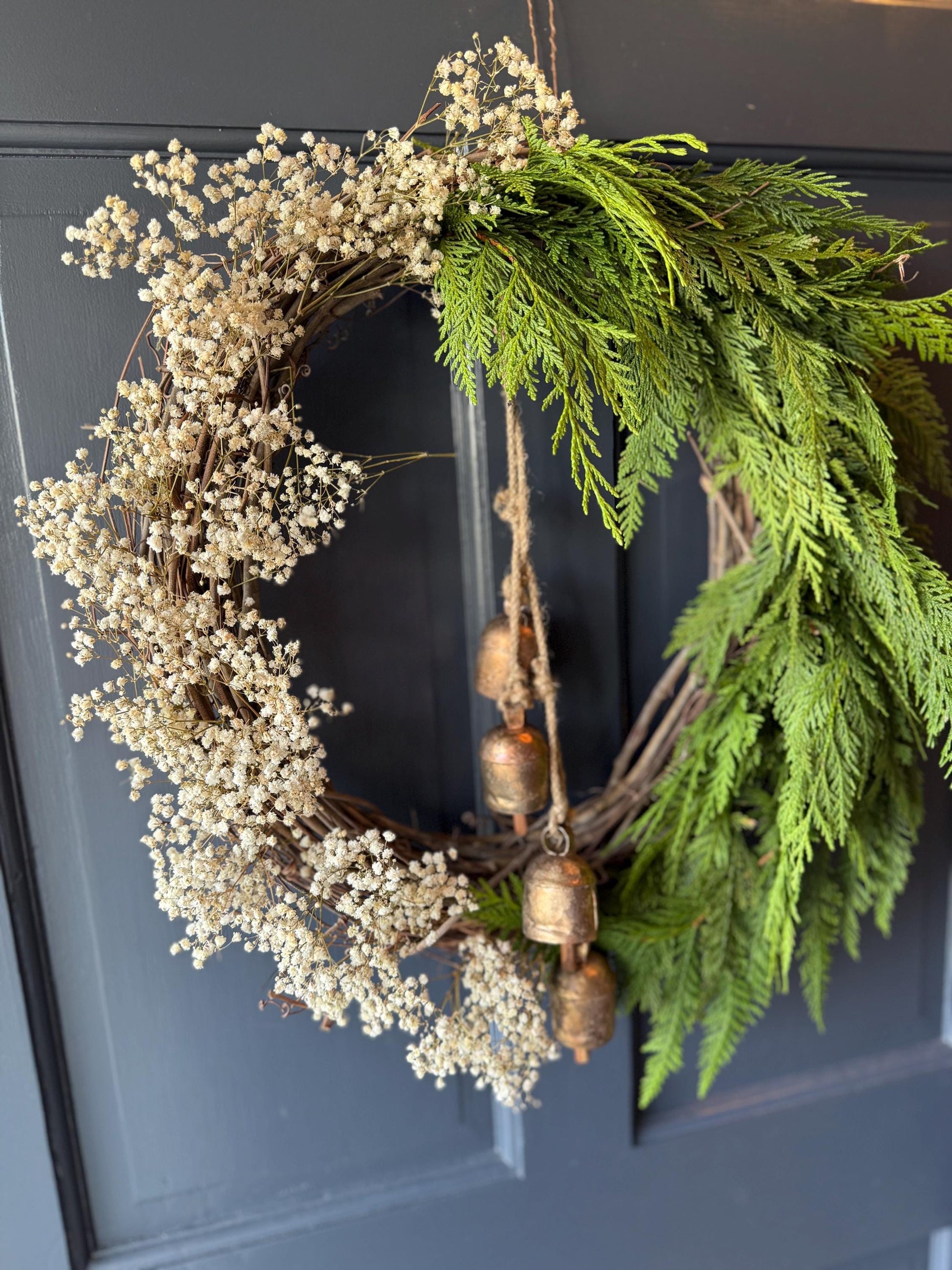 Holiday wreath featuring fresh cedar, preserved baby&#39;s breath and a hanging vintage copper bell cluster. Adorn a wall, mantel or sheltered door; this dried flower wreath is the perfect way to add beauty to your space this holiday season decor.