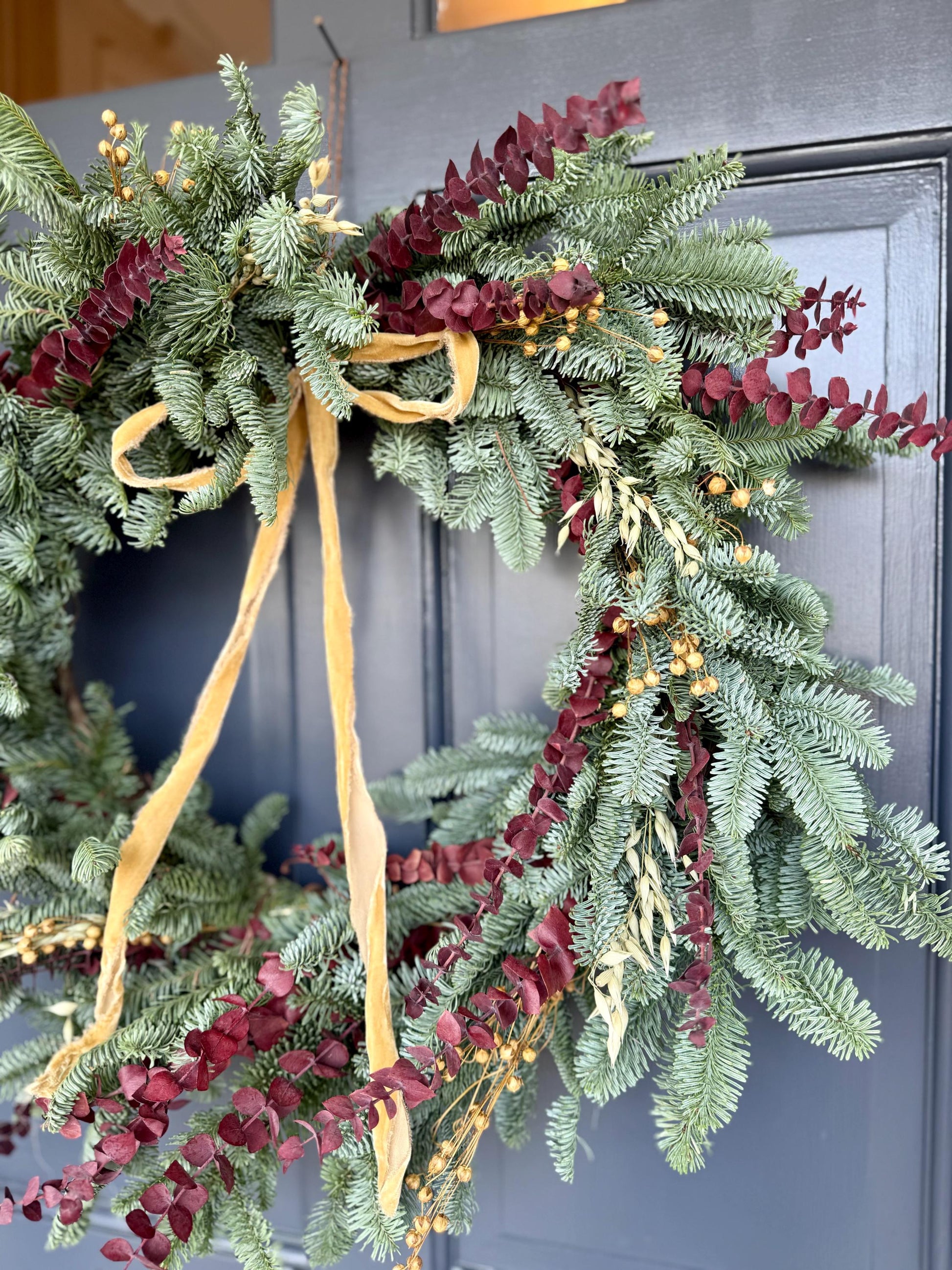 Holiday wreath featuring fresh noble fir, preserved eucalyptus, dried flax and  a gorgeous gold velvet ribbon. 
Adorn a wall, mantel or sheltered door; this fresh, dried and preserved wreath is the perfect way to add beauty to your space.